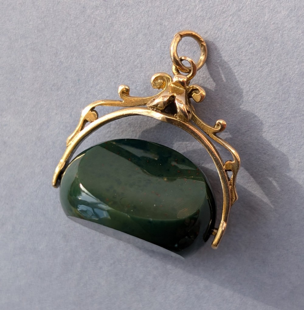 An antique 9ct gold spinning fob pendant featuring a polished dark green bloodstone within an ornate scrolled gold swivel frame. View IV