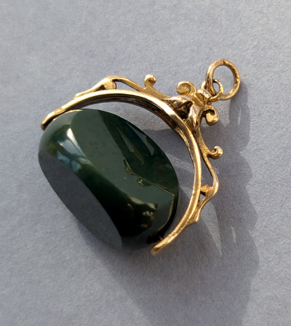 An antique 9ct gold spinning fob pendant featuring a polished dark green bloodstone within an ornate scrolled gold swivel frame. View V