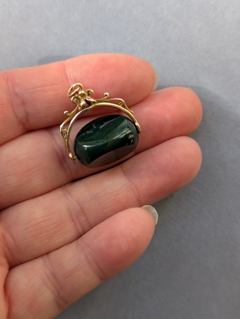 An antique 9ct gold spinning fob pendant featuring a polished dark green bloodstone within an ornate scrolled gold swivel frame. View VI