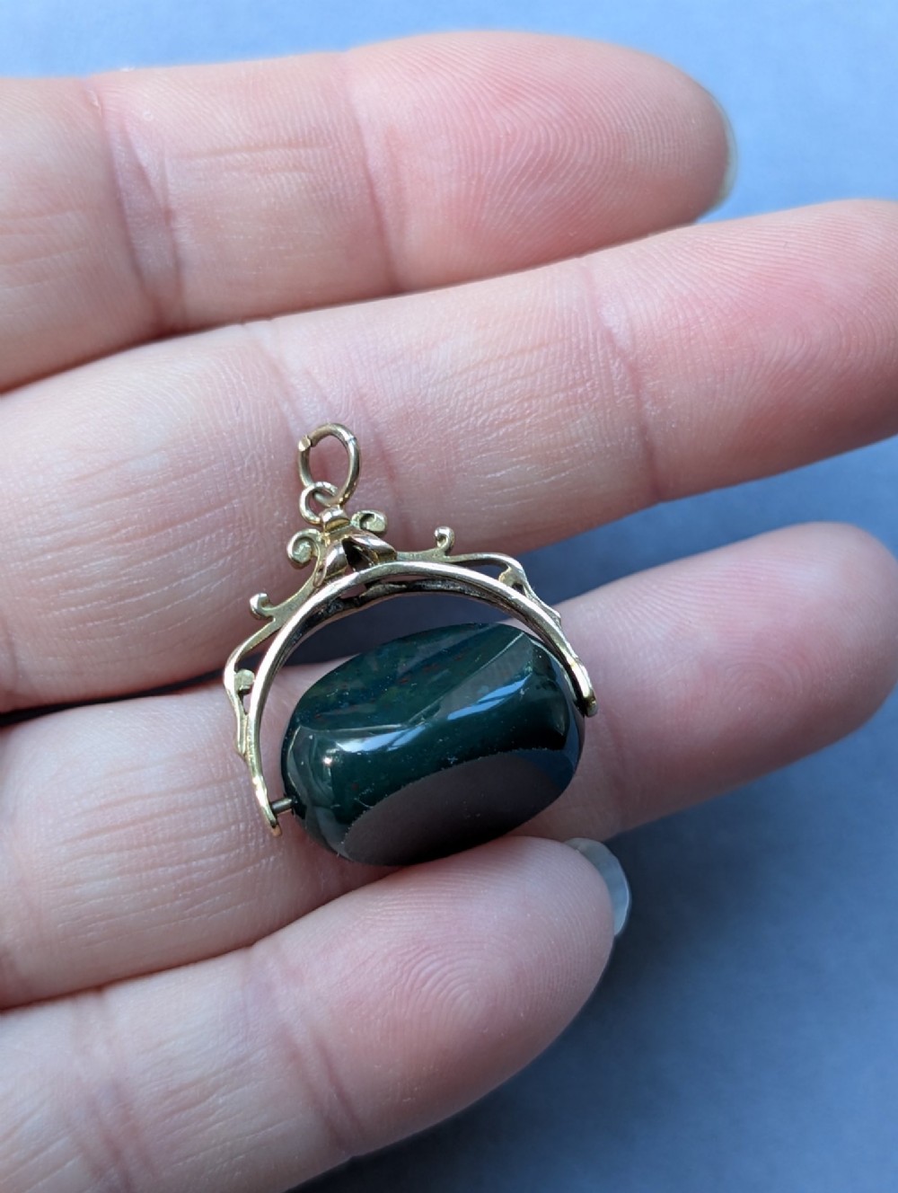 An antique 9ct gold spinning fob pendant featuring a polished dark green bloodstone within an ornate scrolled gold swivel frame. View VII