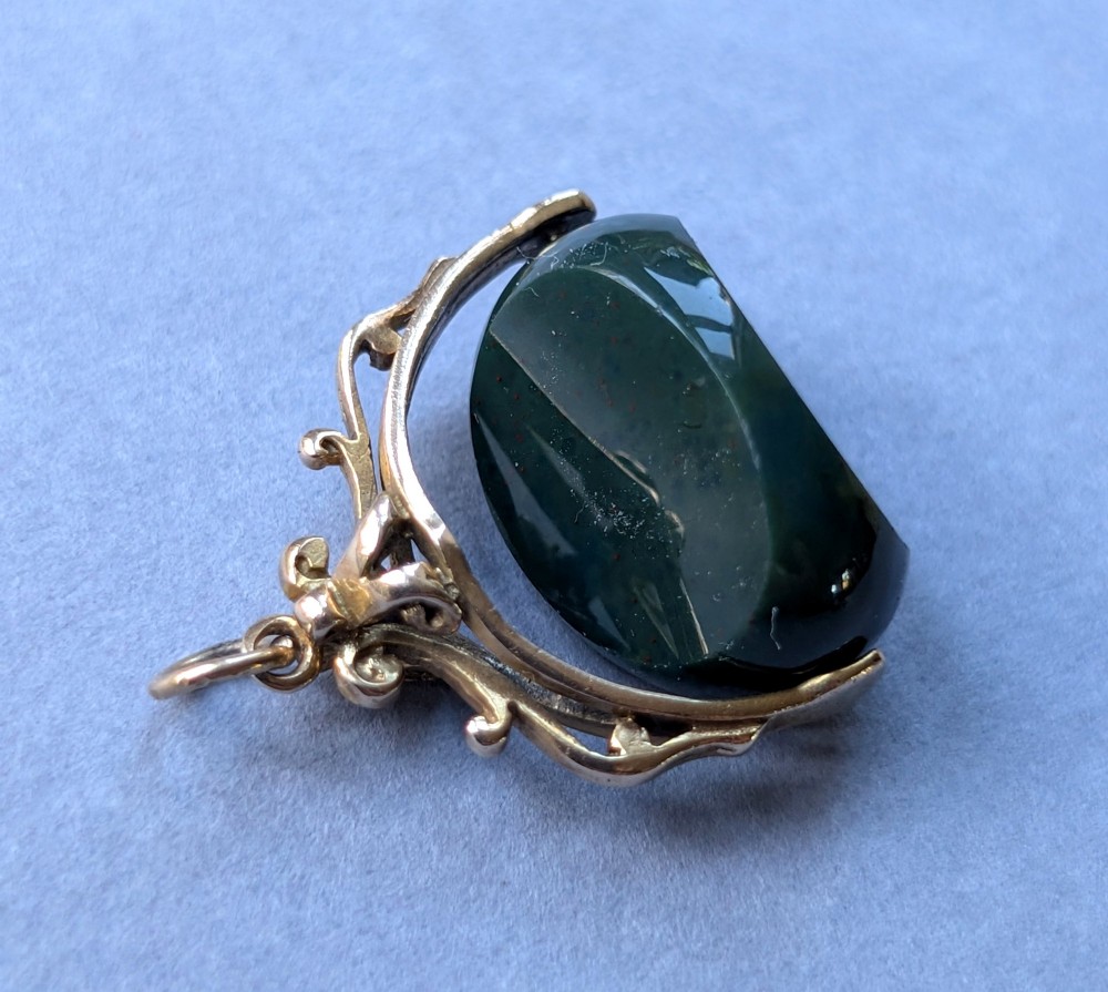 An antique 9ct gold spinning fob pendant featuring a polished dark green bloodstone within an ornate scrolled gold swivel frame. View VIII