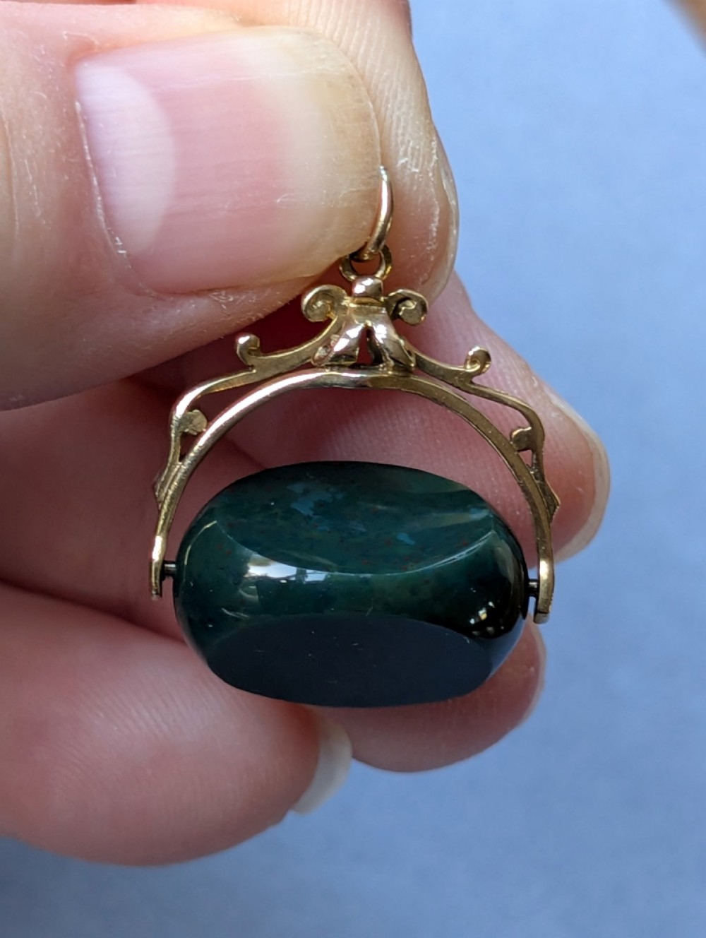 An antique 9ct gold spinning fob pendant featuring a polished dark green bloodstone within an ornate scrolled gold swivel frame. View IX