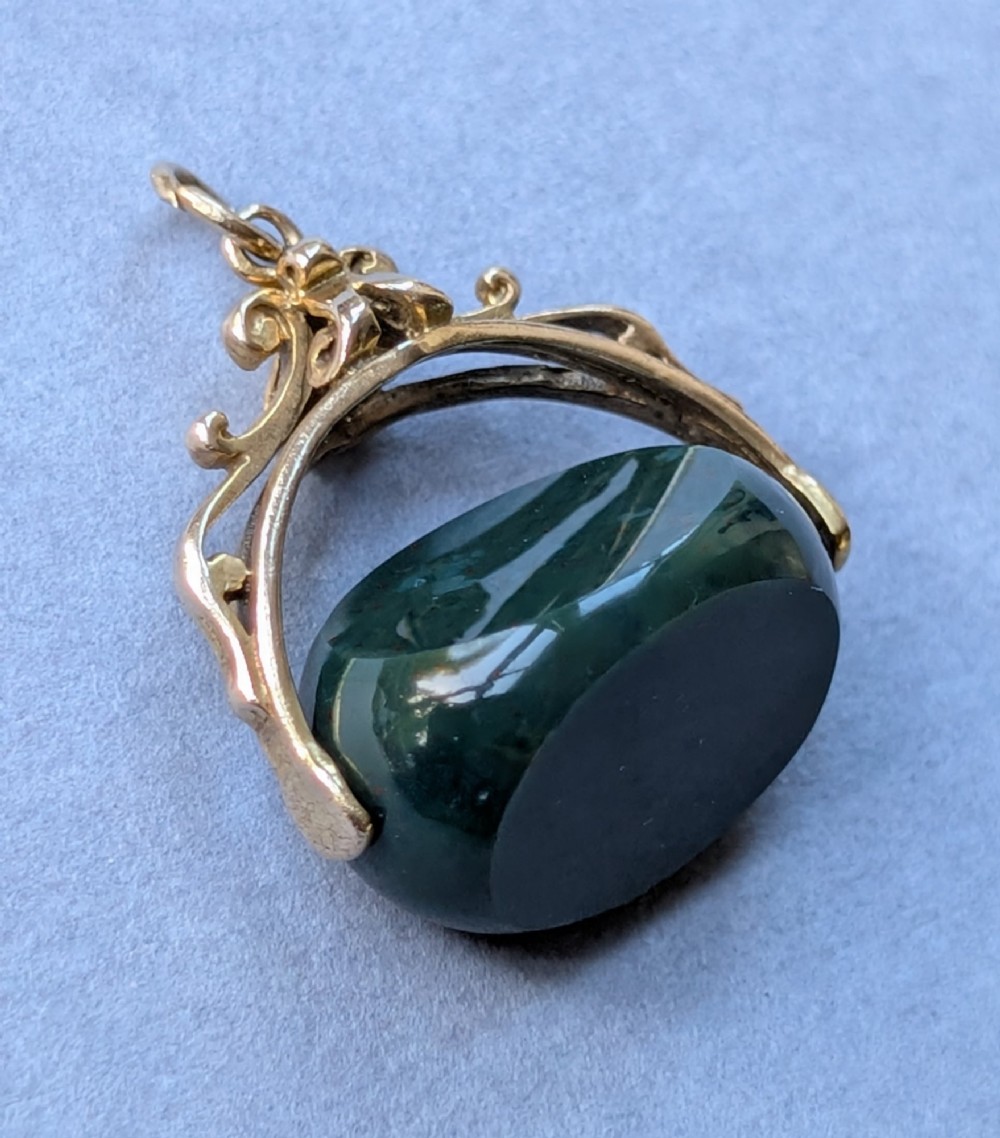 An antique 9ct gold spinning fob pendant featuring a polished dark green bloodstone within an ornate scrolled gold swivel frame. View XI