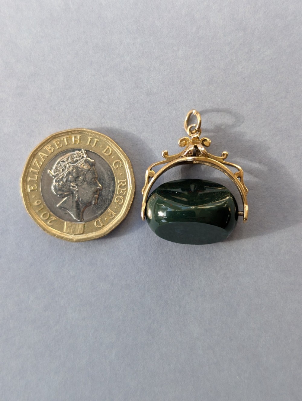 An antique 9ct gold spinning fob pendant featuring a polished dark green bloodstone within an ornate scrolled gold swivel frame. View XII