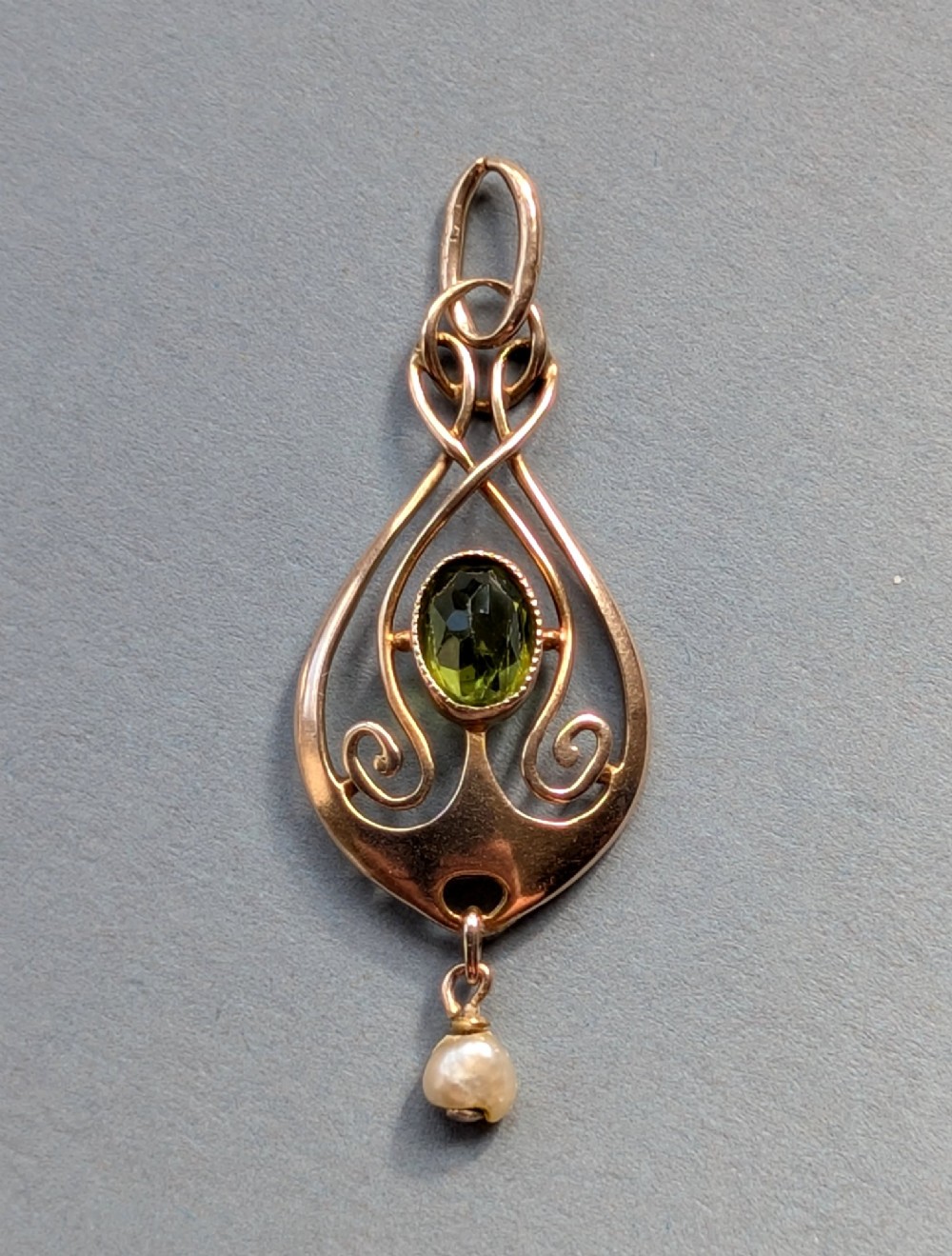 An Edwardian 9ct gold openwork Art Nouveau pendant featuring an oval bezel-set green peridot and a suspended pearl drop. View II