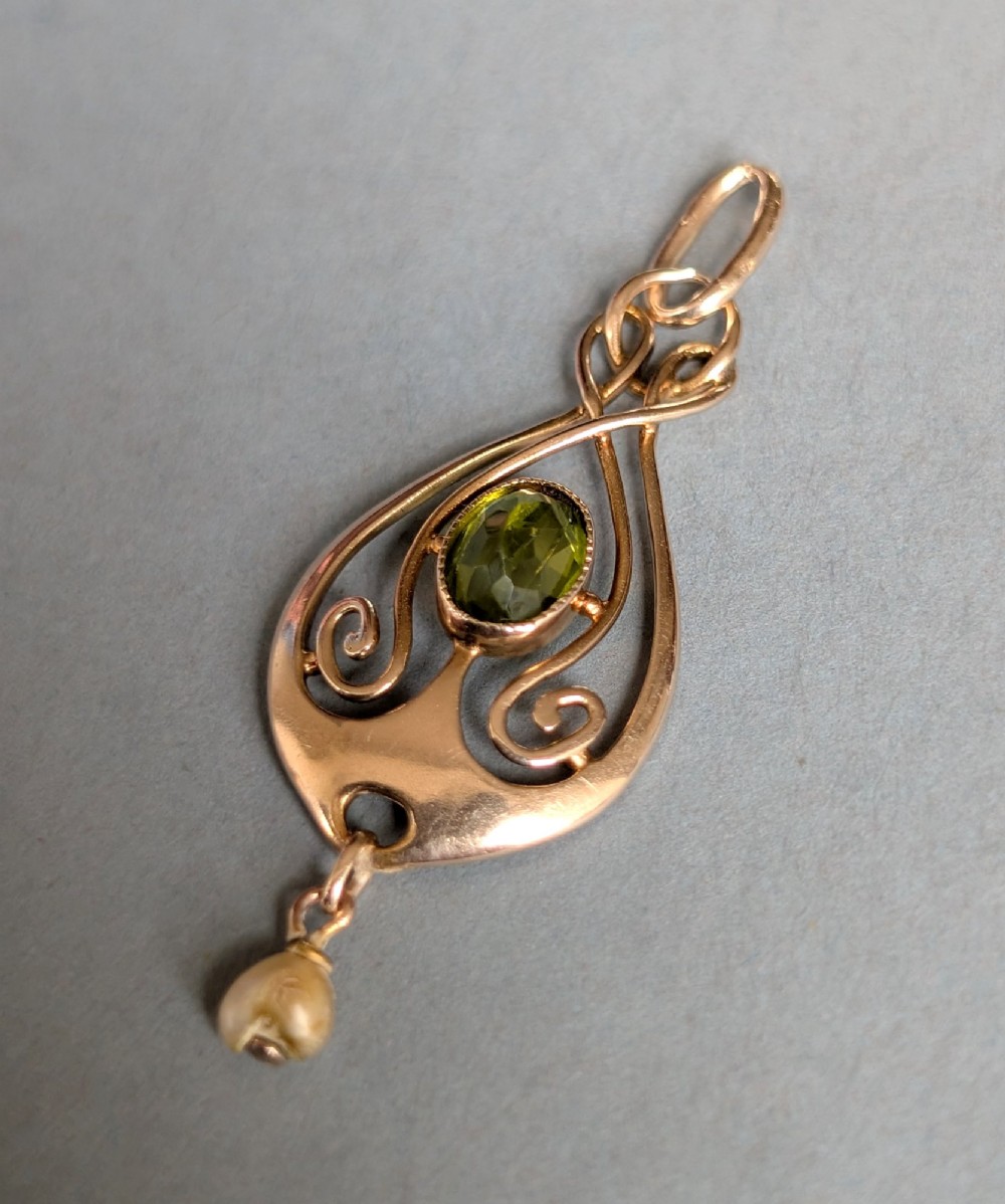 An Edwardian 9ct gold openwork Art Nouveau pendant featuring an oval bezel-set green peridot and a suspended pearl drop. View III