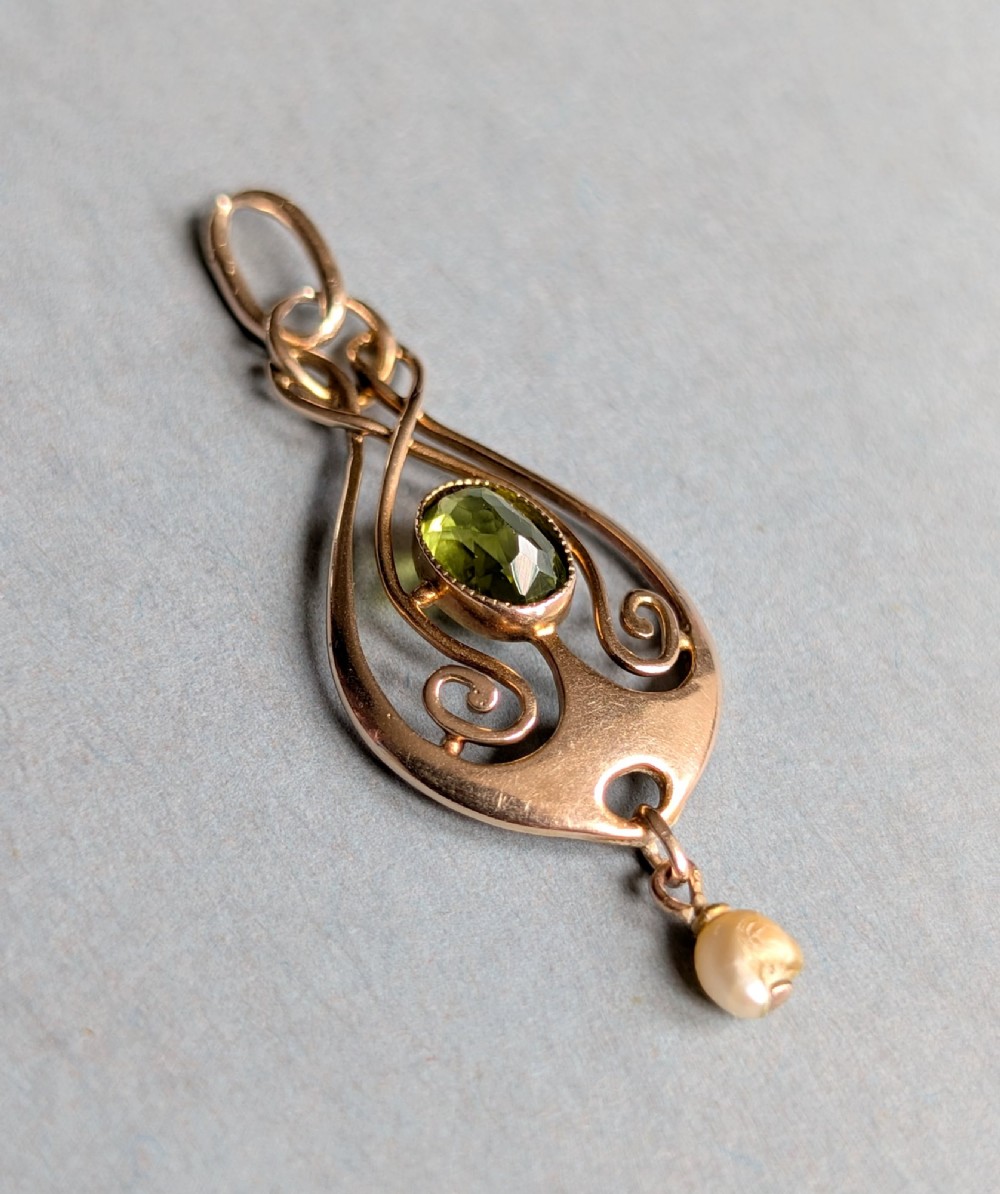 An Edwardian 9ct gold openwork Art Nouveau pendant featuring an oval bezel-set green peridot and a suspended pearl drop. View IV