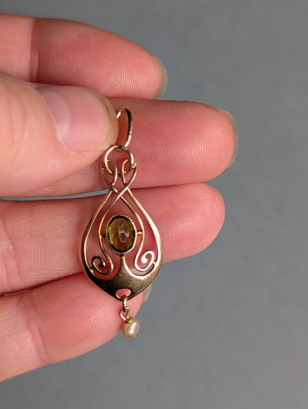 An Edwardian 9ct gold openwork Art Nouveau pendant featuring an oval bezel-set green peridot and a suspended pearl drop. View VI