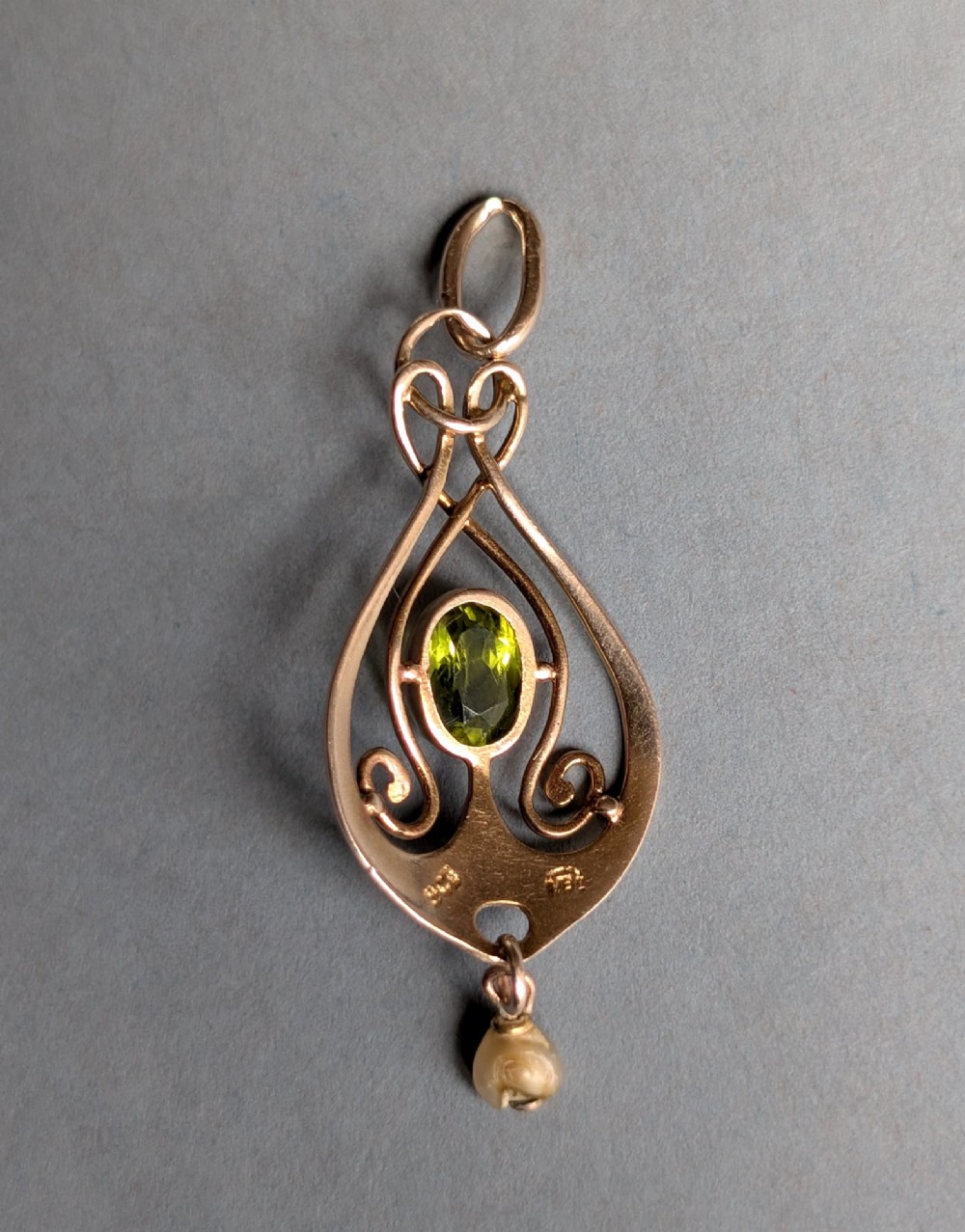 An Edwardian 9ct gold openwork Art Nouveau pendant featuring an oval bezel-set green peridot and a suspended pearl drop. View VII