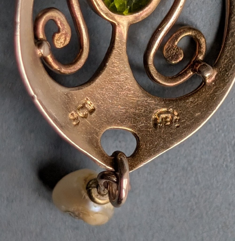 An Edwardian 9ct gold openwork Art Nouveau pendant featuring an oval bezel-set green peridot and a suspended pearl drop. View VIII