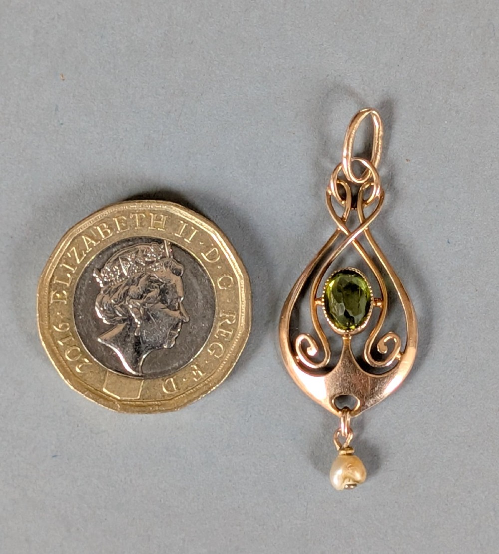 An Edwardian 9ct gold openwork Art Nouveau pendant featuring an oval bezel-set green peridot and a suspended pearl drop. View IX