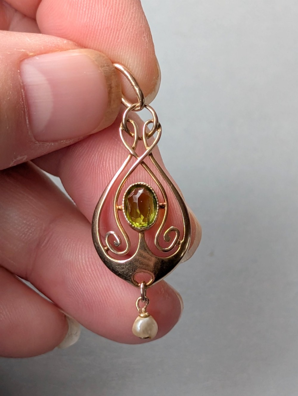 An Edwardian 9ct gold openwork Art Nouveau pendant featuring an oval bezel-set green peridot and a suspended pearl drop. View XI