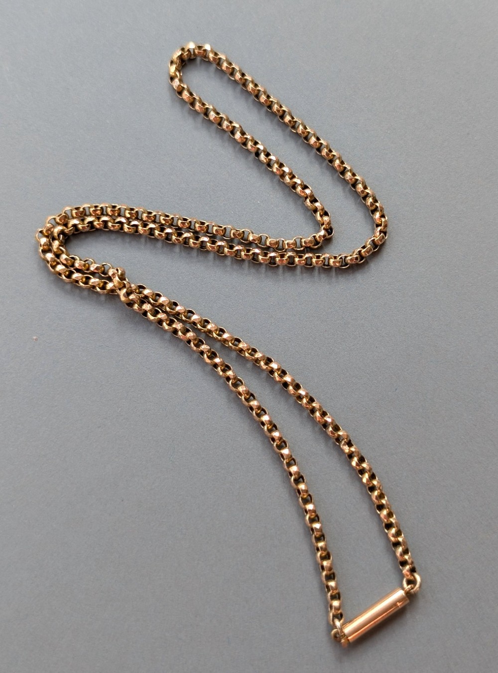 An antique 9ct yellow gold belcher chain laid on a plain background showing interlocking rounded links and a barrel fastener.