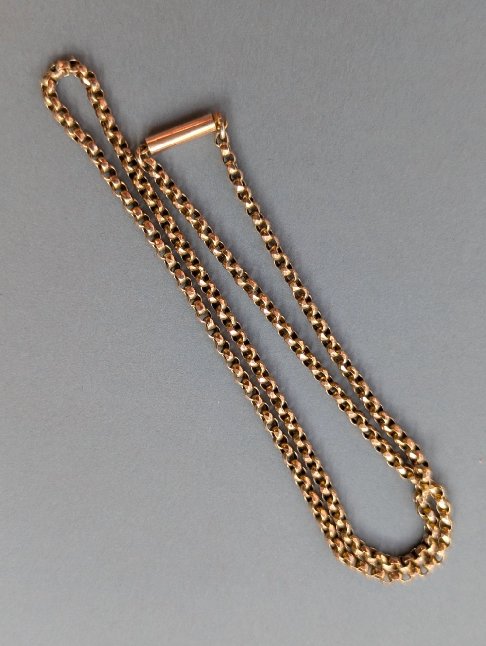 An antique 9ct yellow gold belcher chain laid on a plain background showing interlocking rounded links and a barrel fastener. View II