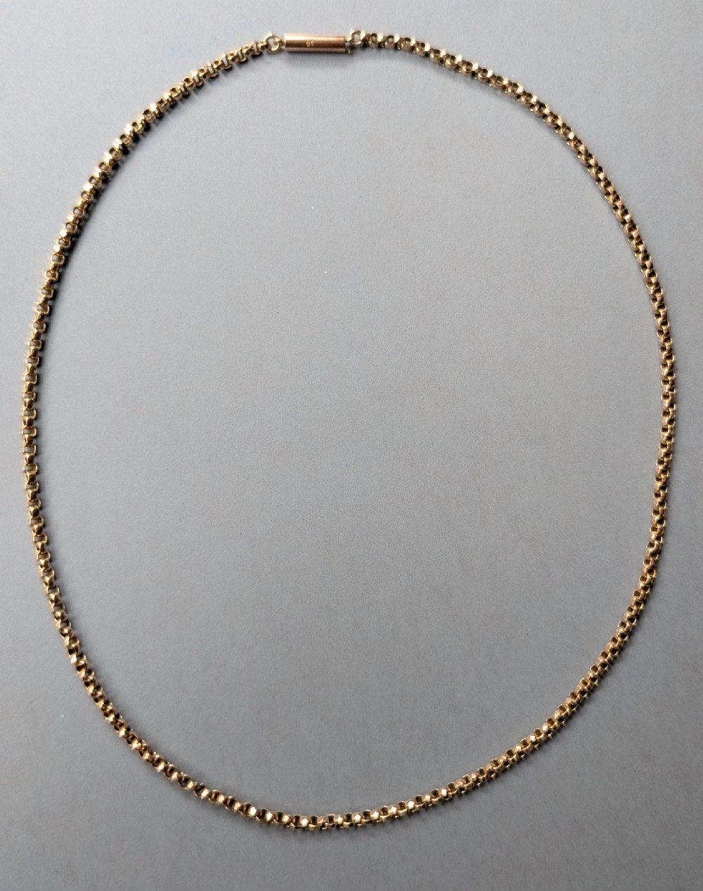 An antique 9ct yellow gold belcher chain laid on a plain background showing interlocking rounded links and a barrel fastener. View III