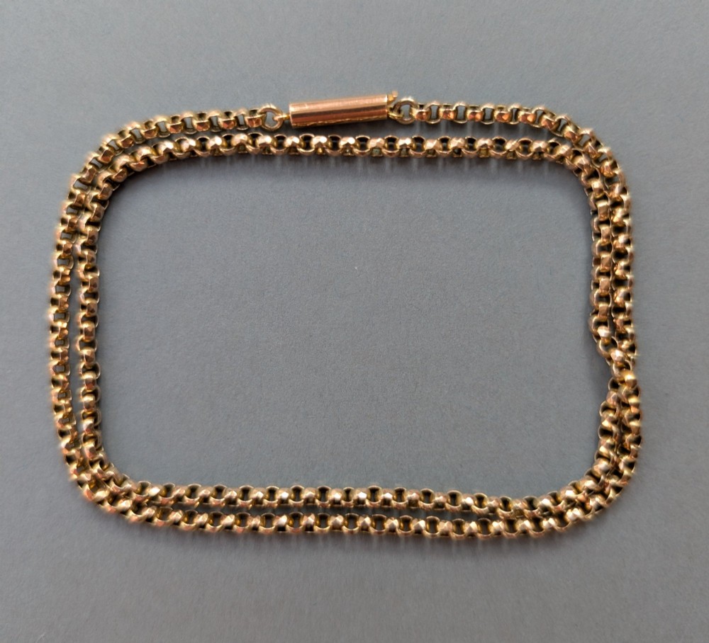 An antique 9ct yellow gold belcher chain laid on a plain background showing interlocking rounded links and a barrel fastener. View V