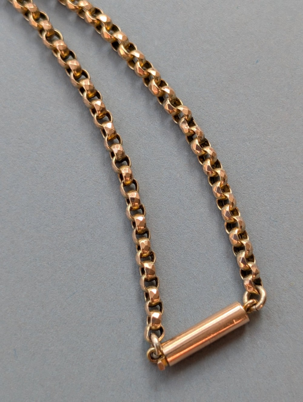 An antique 9ct yellow gold belcher chain laid on a plain background showing interlocking rounded links and a barrel fastener. View VII
