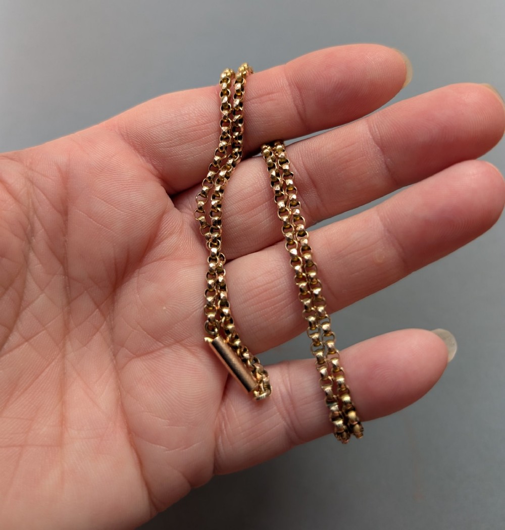 An antique 9ct yellow gold belcher chain laid on a plain background showing interlocking rounded links and a barrel fastener. View VIII