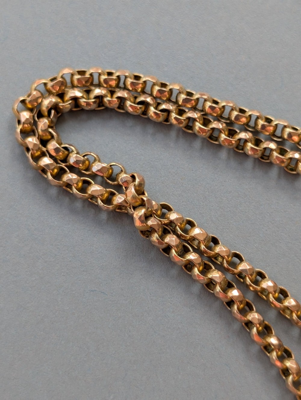 An antique 9ct yellow gold belcher chain laid on a plain background showing interlocking rounded links and a barrel fastener. View IX