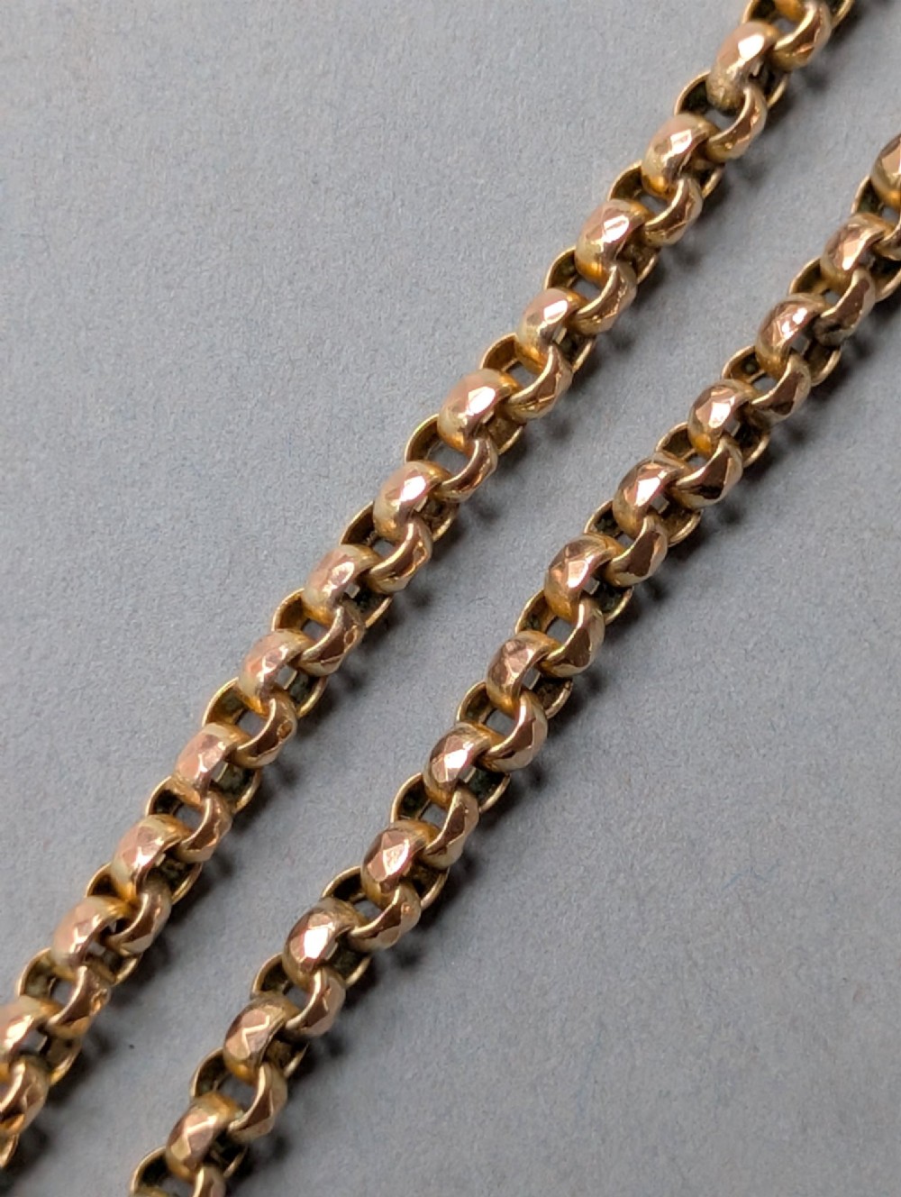 An antique 9ct yellow gold belcher chain laid on a plain background showing interlocking rounded links and a barrel fastener. View X