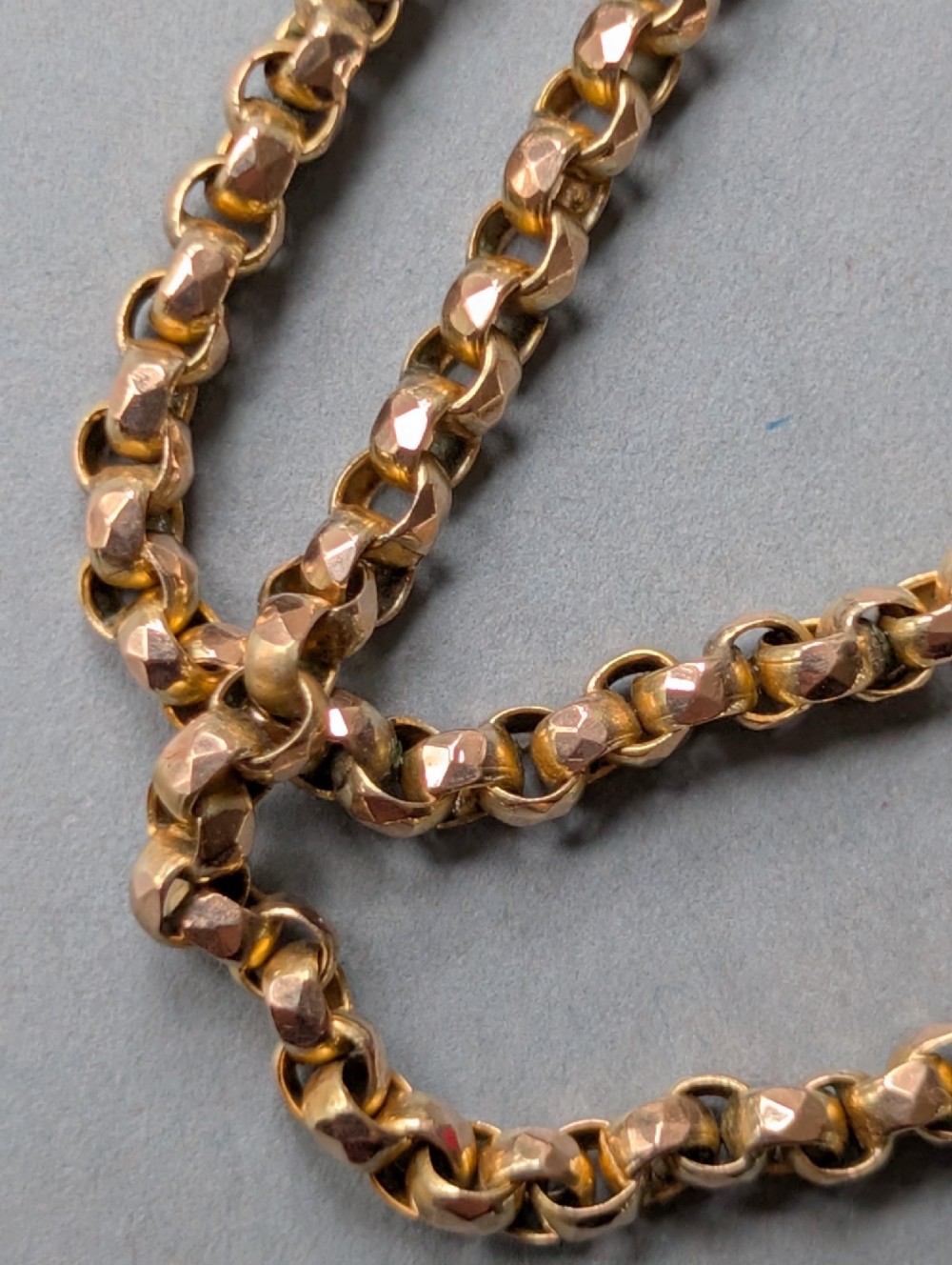 An antique 9ct yellow gold belcher chain laid on a plain background showing interlocking rounded links and a barrel fastener. View XI