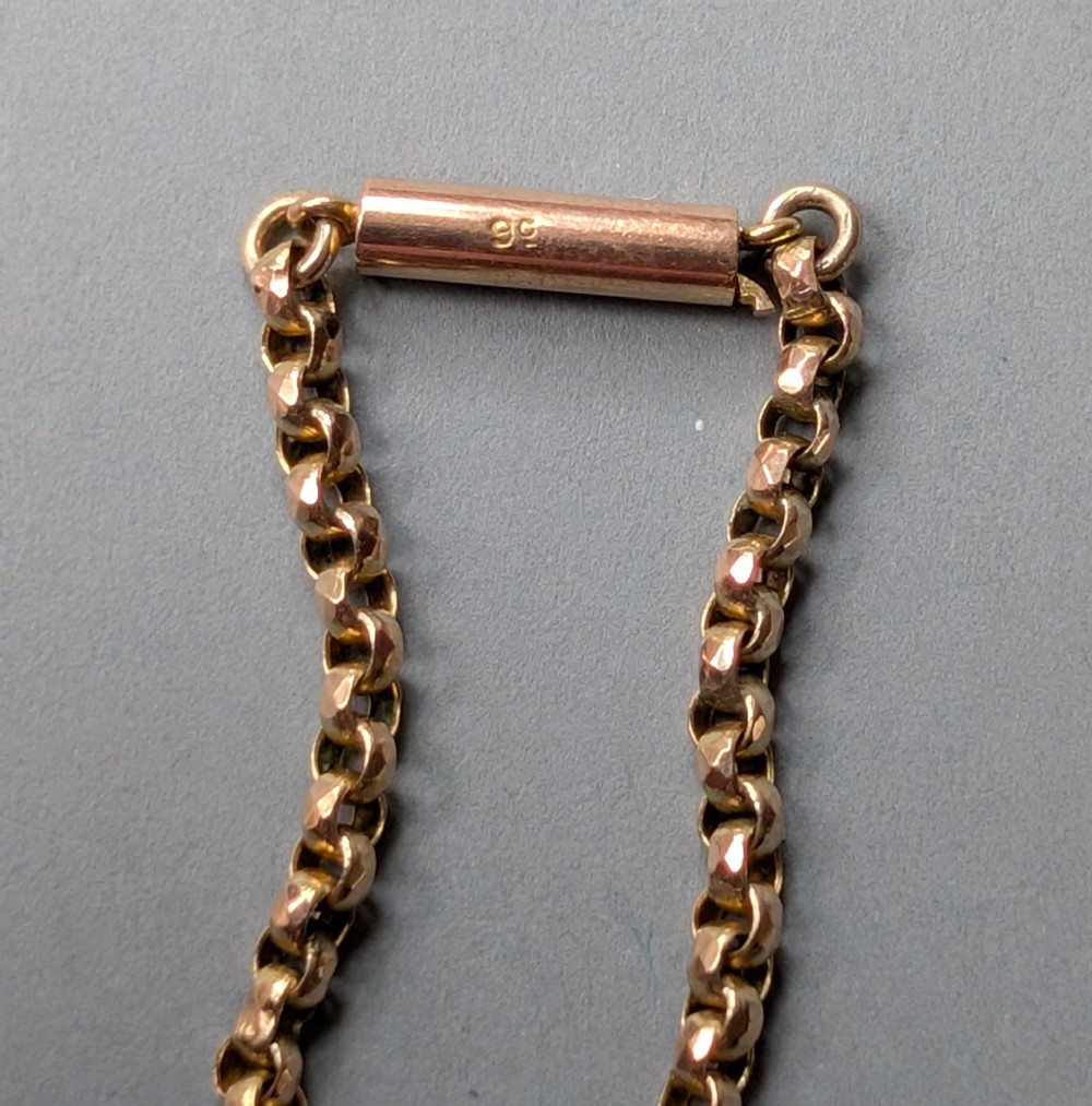 An antique 9ct yellow gold belcher chain laid on a plain background showing interlocking rounded links and a barrel fastener. View XII