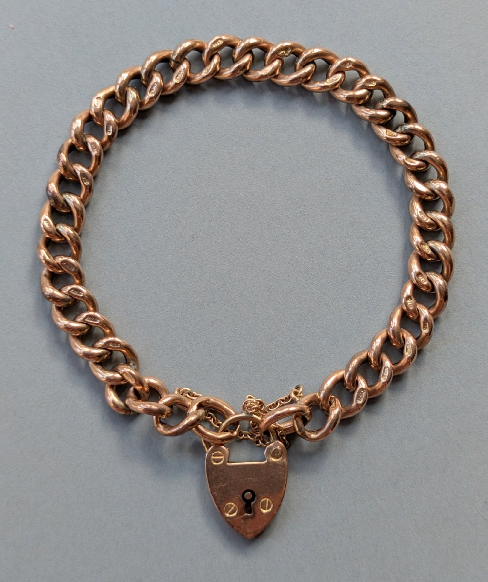 An Edwardian 9ct rose gold curb link chain bracelet featuring a heart-shaped padlock clasp and safety chain.