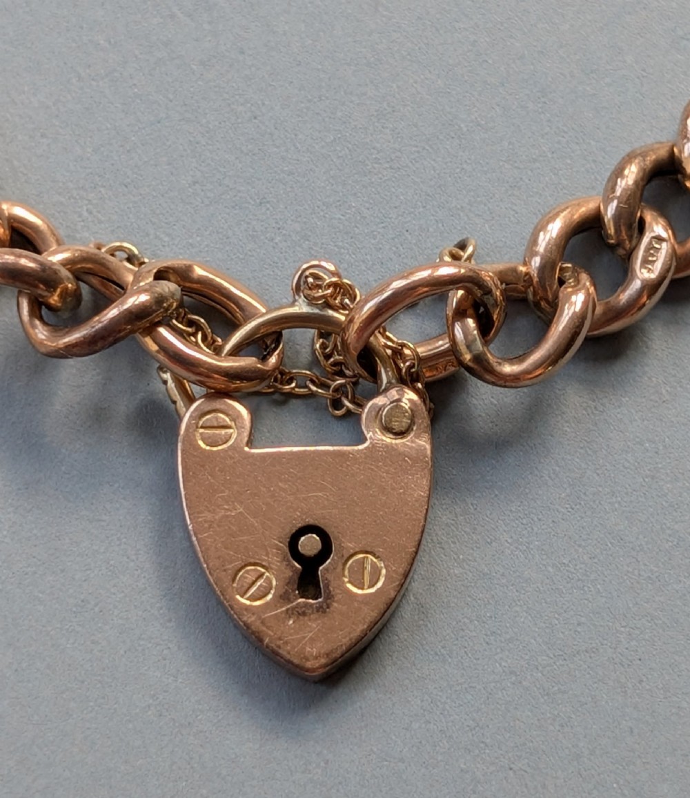 An Edwardian 9ct rose gold curb link chain bracelet featuring a heart-shaped padlock clasp and safety chain. View IV