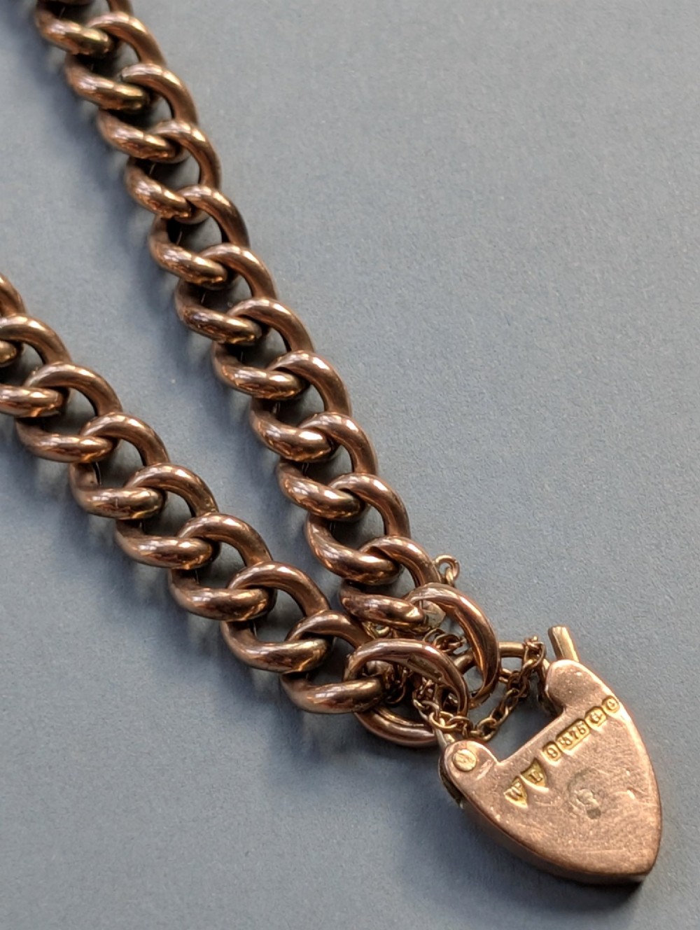 An Edwardian 9ct rose gold curb link chain bracelet featuring a heart-shaped padlock clasp and safety chain. View X
