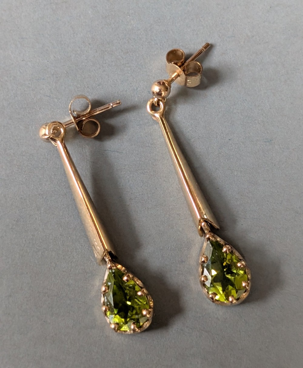 A pair of antique 9ct gold drop earrings featuring tapered bars and pear-cut green peridot gemstones suspended from ball posts. View IV