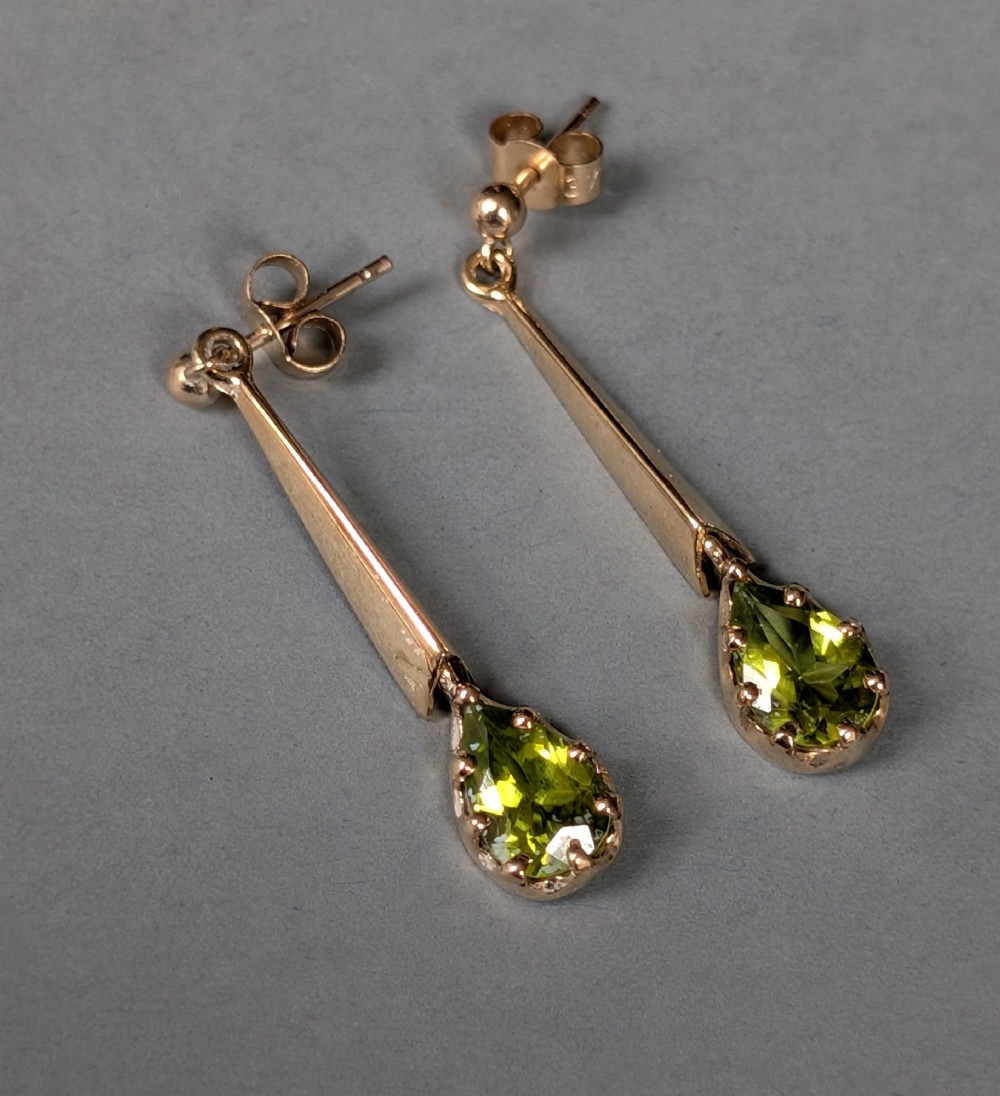A pair of antique 9ct gold drop earrings featuring tapered bars and pear-cut green peridot gemstones suspended from ball posts. View V