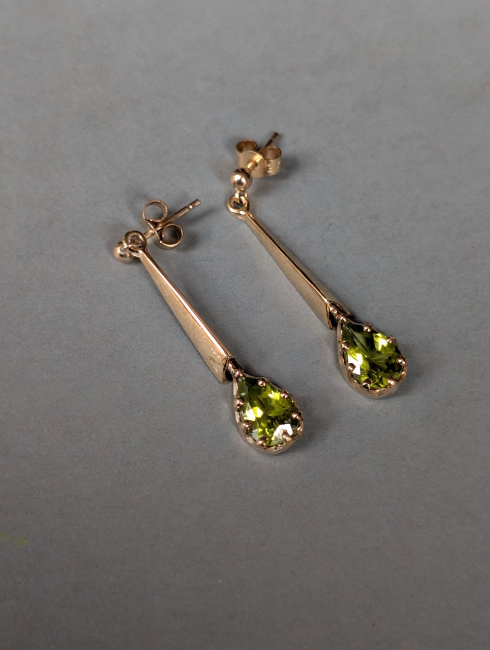 A pair of antique 9ct gold drop earrings featuring tapered bars and pear-cut green peridot gemstones suspended from ball posts. View VI