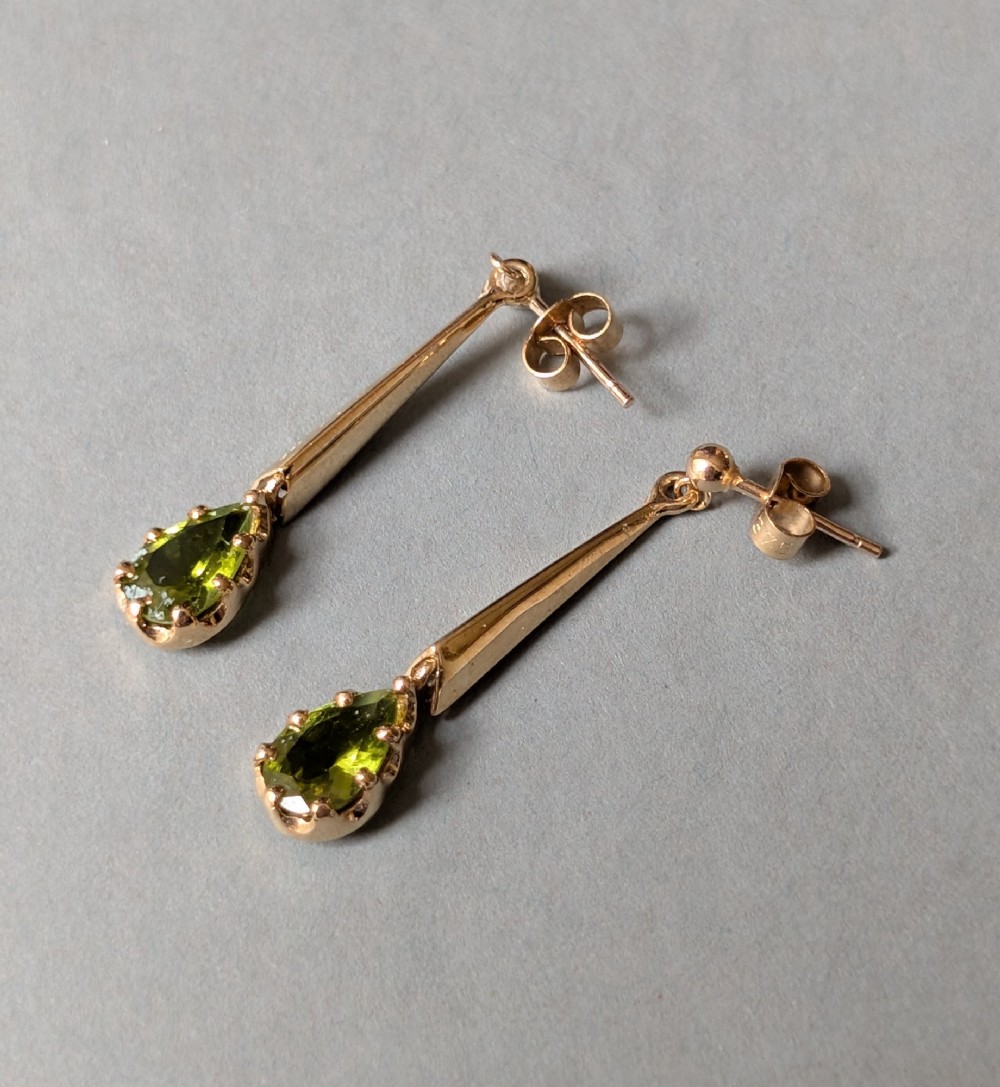A pair of antique 9ct gold drop earrings featuring tapered bars and pear-cut green peridot gemstones suspended from ball posts. View VIII