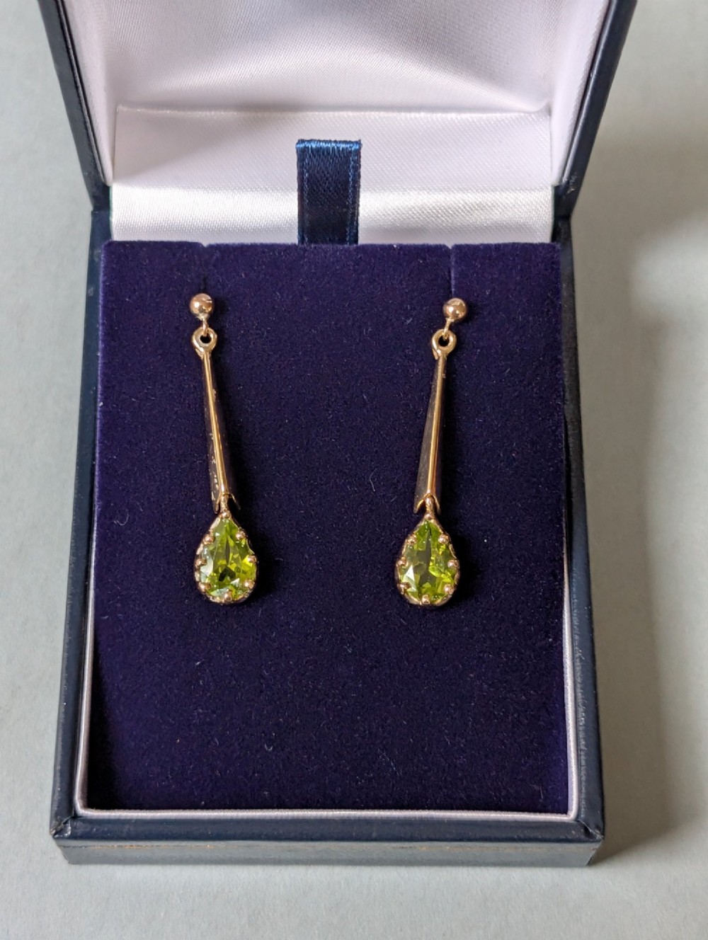 A pair of antique 9ct gold drop earrings featuring tapered bars and pear-cut green peridot gemstones suspended from ball posts. View IX