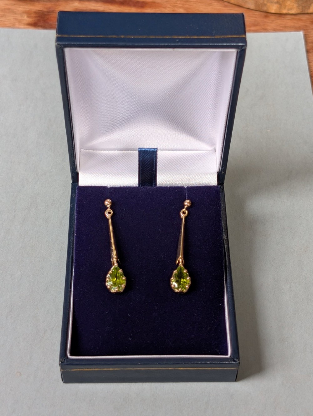 A pair of antique 9ct gold drop earrings featuring tapered bars and pear-cut green peridot gemstones suspended from ball posts. View X
