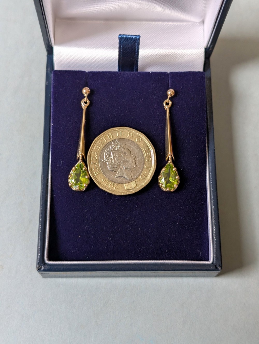 A pair of antique 9ct gold drop earrings featuring tapered bars and pear-cut green peridot gemstones suspended from ball posts. View XI
