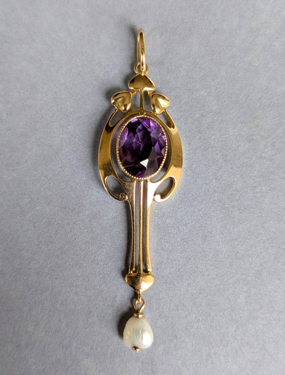 An Art Nouveau 15ct gold drop pendant featuring a central oval faceted purple amethyst framed by stylised leaf motifs with a suspended pearl at the base. View II