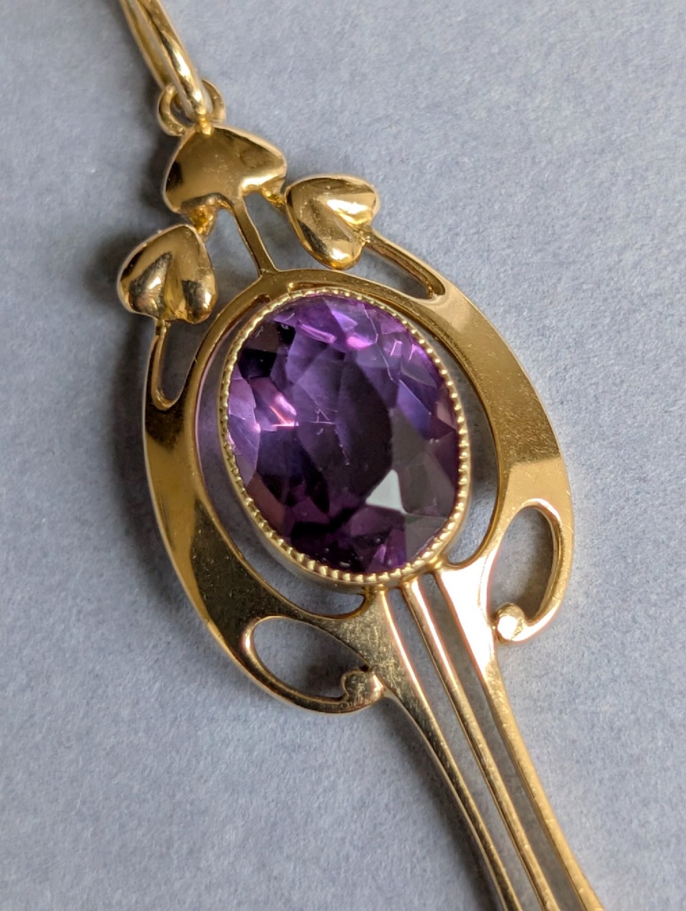 An Art Nouveau 15ct gold drop pendant featuring a central oval faceted purple amethyst framed by stylised leaf motifs with a suspended pearl at the base. View III