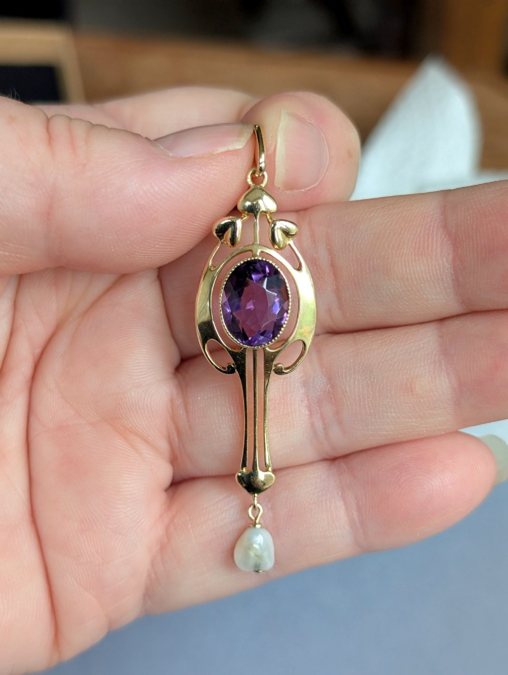 An Art Nouveau 15ct gold drop pendant featuring a central oval faceted purple amethyst framed by stylised leaf motifs with a suspended pearl at the base. View VI