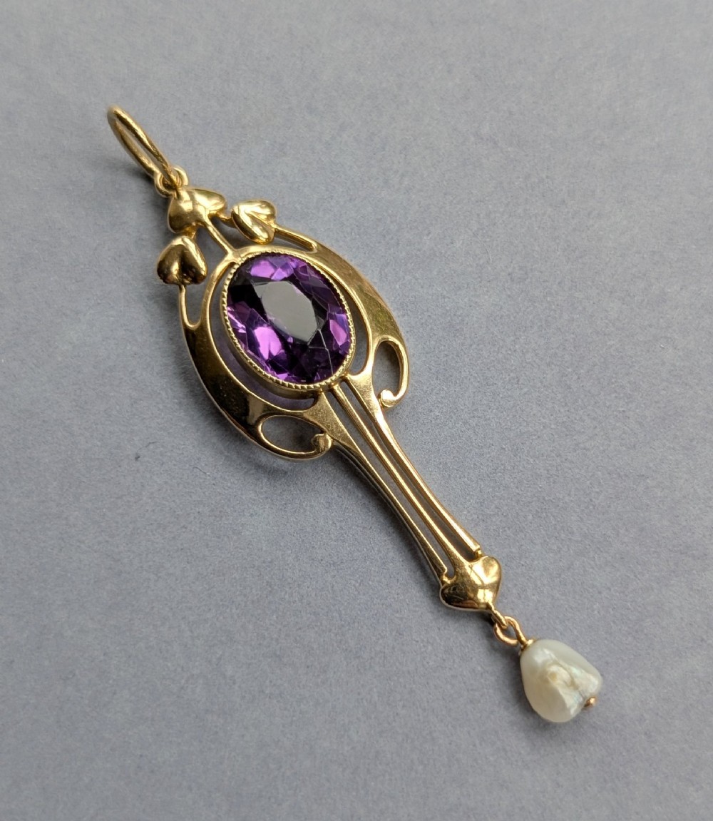 An Art Nouveau 15ct gold drop pendant featuring a central oval faceted purple amethyst framed by stylised leaf motifs with a suspended pearl at the base. View VIII