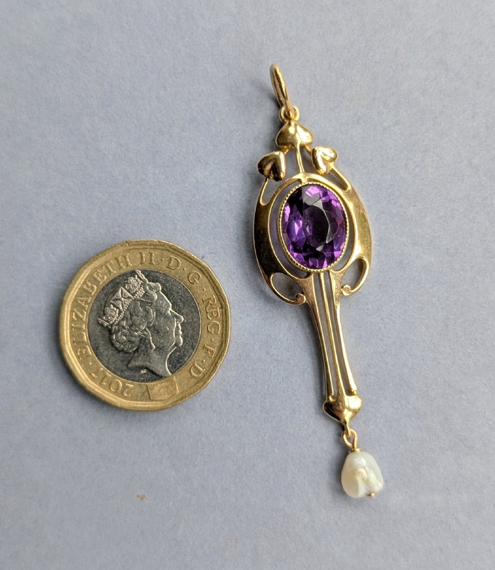 An Art Nouveau 15ct gold drop pendant featuring a central oval faceted purple amethyst framed by stylised leaf motifs with a suspended pearl at the base. View IX