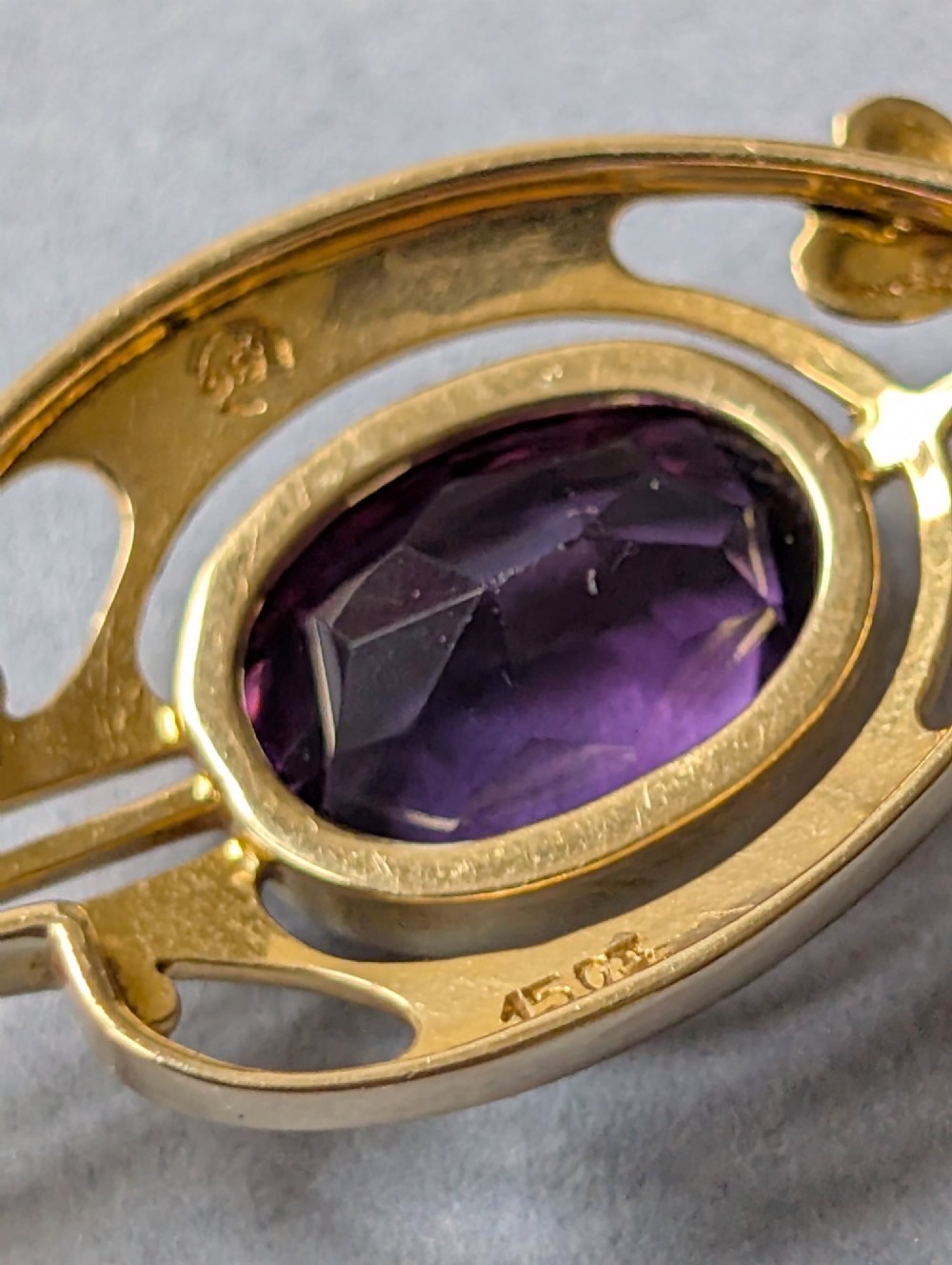An Art Nouveau 15ct gold drop pendant featuring a central oval faceted purple amethyst framed by stylised leaf motifs with a suspended pearl at the base. View X