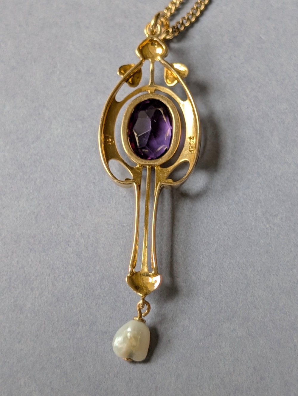 An Art Nouveau 15ct gold drop pendant featuring a central oval faceted purple amethyst framed by stylised leaf motifs with a suspended pearl at the base. View XII