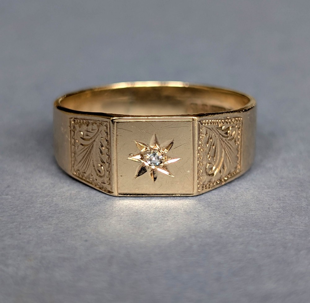 A vintage 9ct yellow gold gents signet ring featuring a star-set central stone and foliate engraved shoulders.