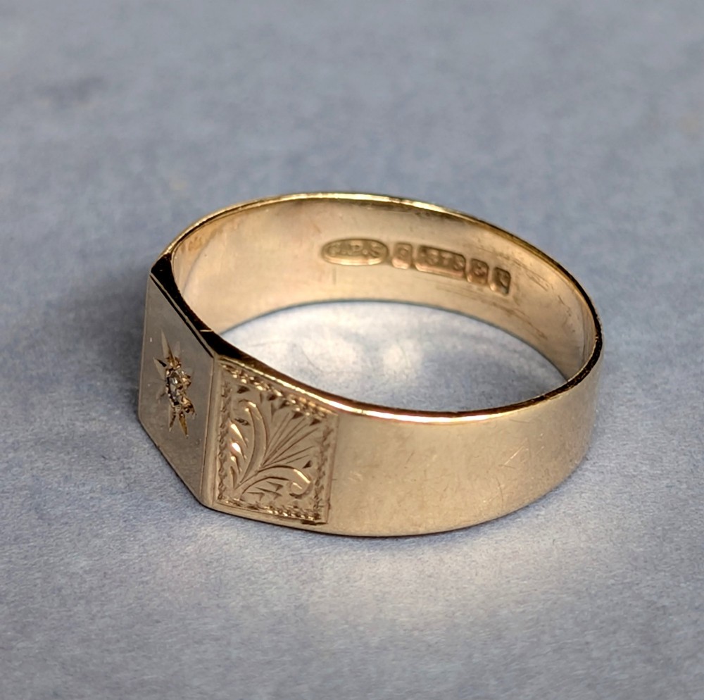 A vintage 9ct yellow gold gents signet ring featuring a star-set central stone and foliate engraved shoulders. View IV