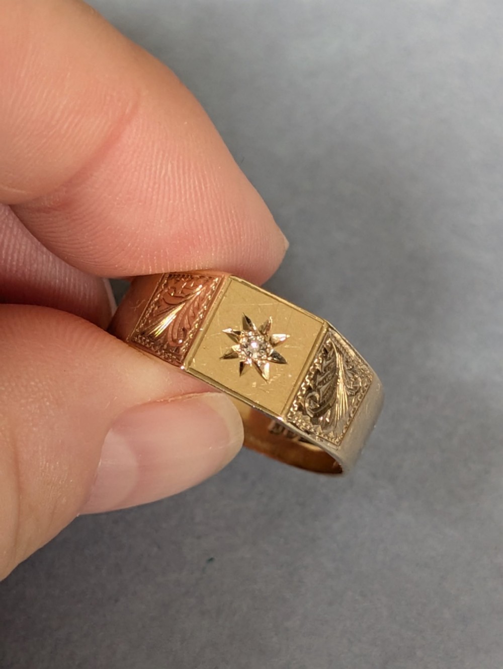 A vintage 9ct yellow gold gents signet ring featuring a star-set central stone and foliate engraved shoulders. View VI