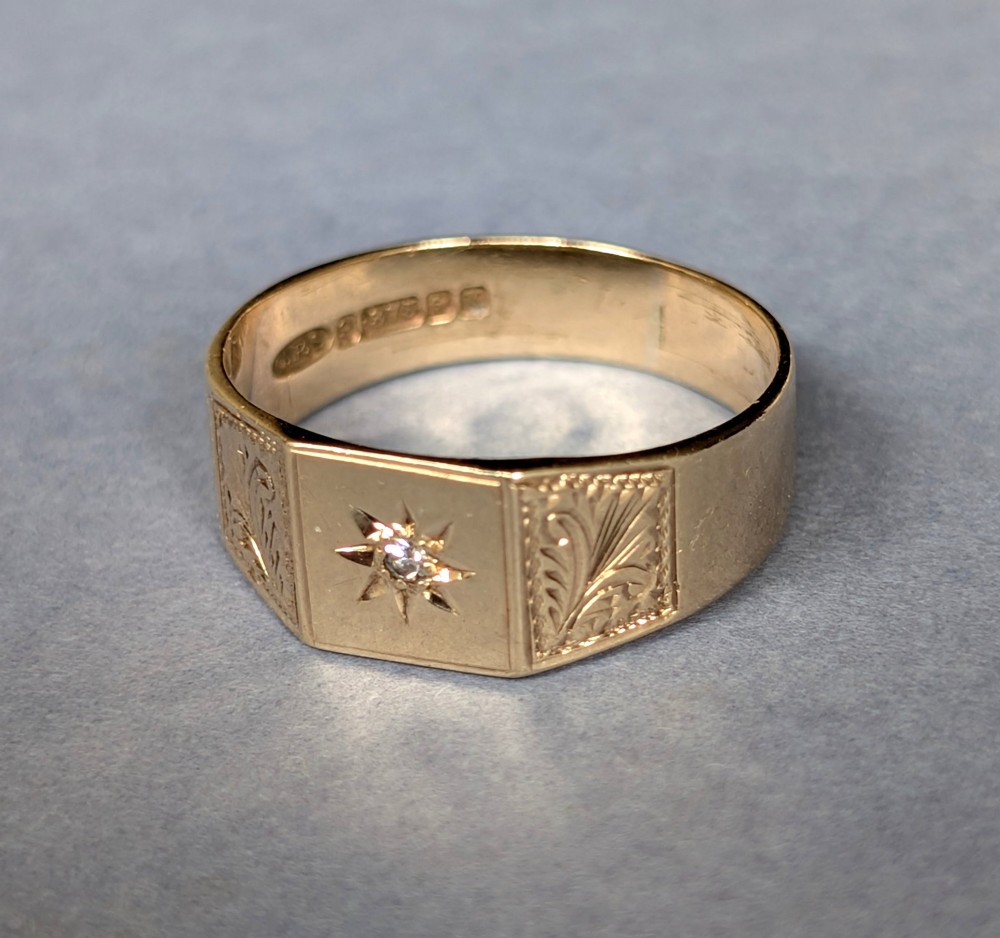 A vintage 9ct yellow gold gents signet ring featuring a star-set central stone and foliate engraved shoulders. View IX
