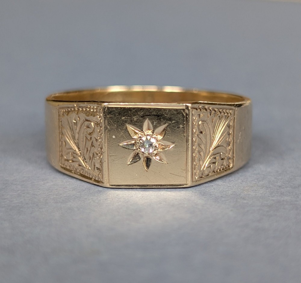 A vintage 9ct yellow gold gents signet ring featuring a star-set central stone and foliate engraved shoulders. View X