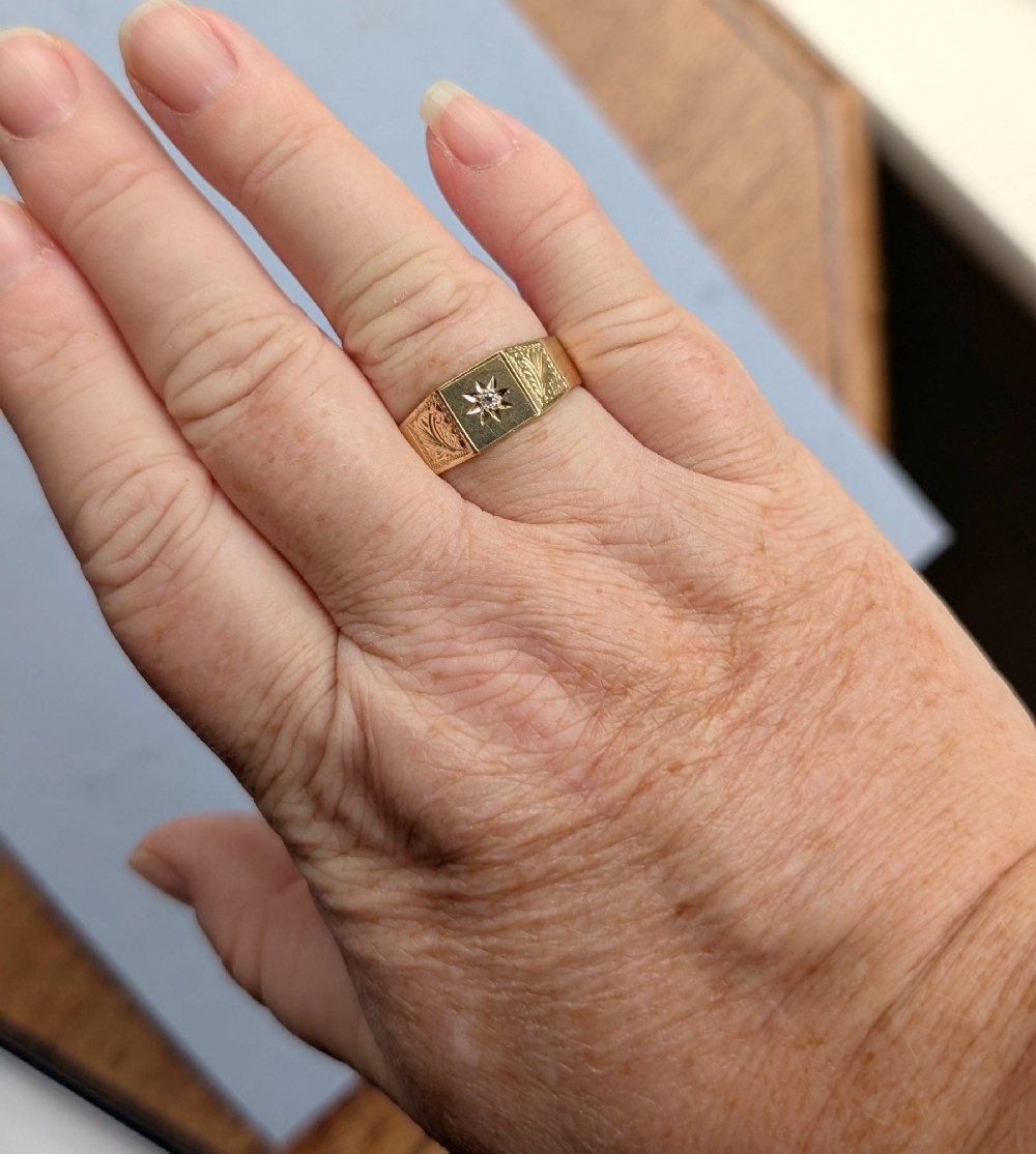 A vintage 9ct yellow gold gents signet ring featuring a star-set central stone and foliate engraved shoulders. View XI
