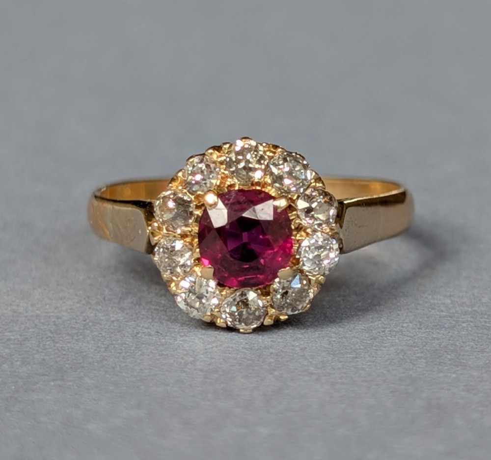 An antique 18ct gold cluster ring featuring a central faceted red ruby surrounded by ten round diamonds. View II